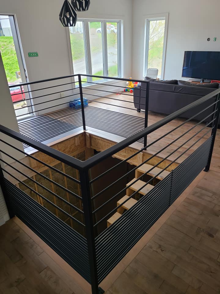 A living room with a staircase and a black railing.