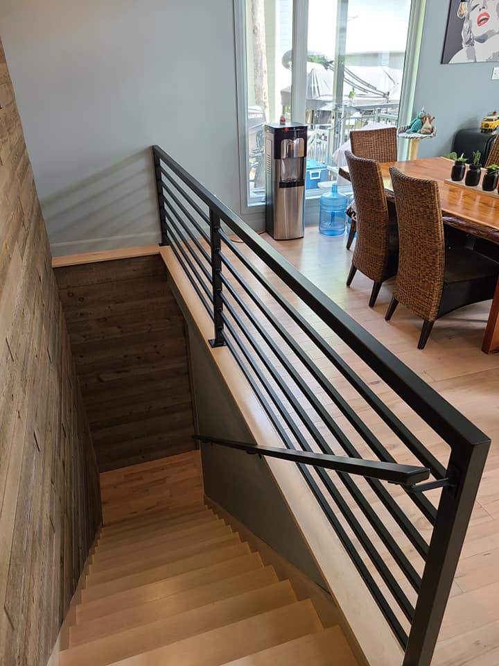 A wooden staircase with a metal railing leading to a dining room.