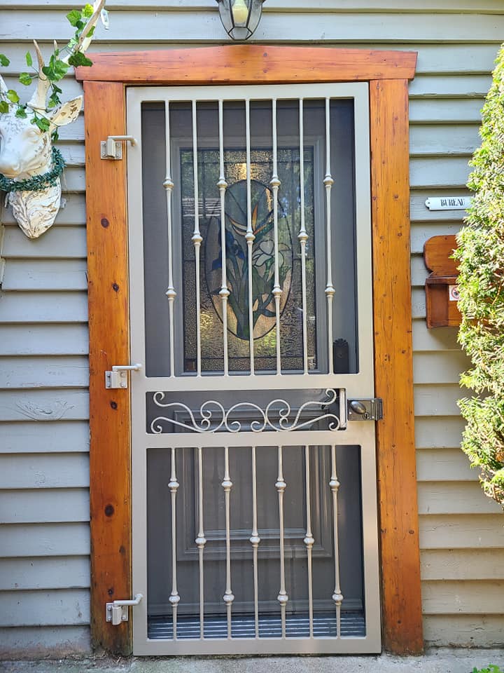 A screen door with a wooden frame is on the side of a house.