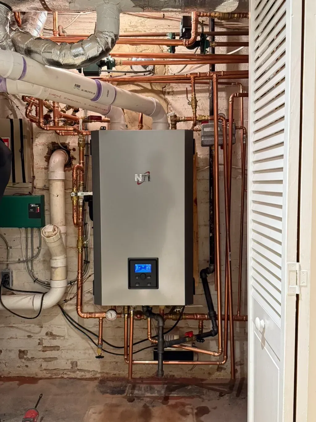 A new silver heating unit in a utility room with copper pipes and ventilation.