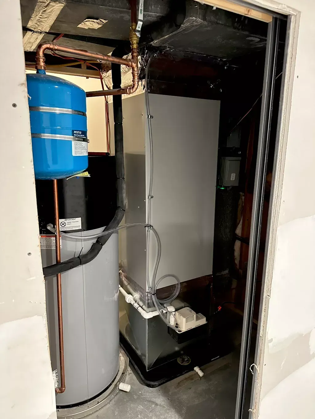 A water heater, blue pressure tank, and a large gray appliance are in a utility closet. Copper pipes are visible.