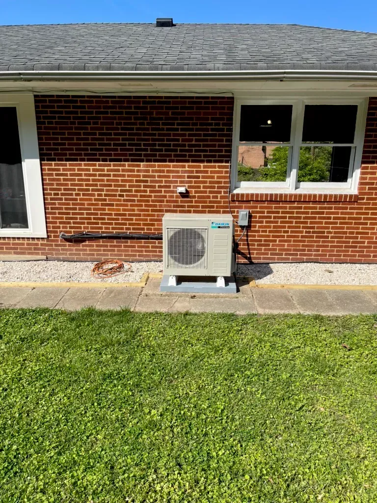 HVAC unit outside a brick building with white trim and windows, set on a concrete pad.