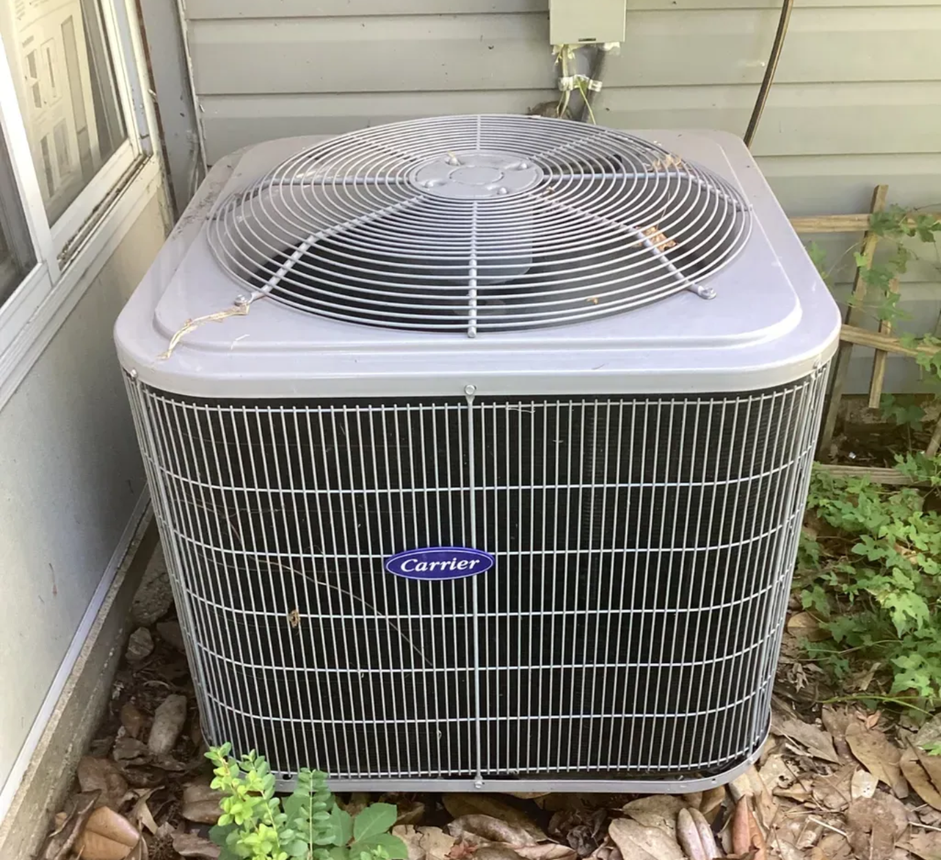 An air conditioning unit outside a building with a fan on top and a Carrier logo on the front.