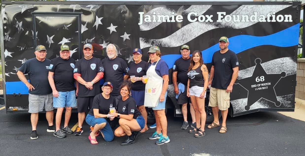 A group of people standing in front of a jaimie cox foundation trailer.