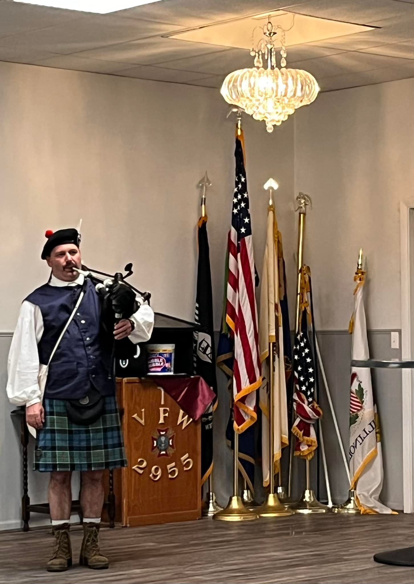 A man in a kilt is playing a bagpipe in a room with flags.