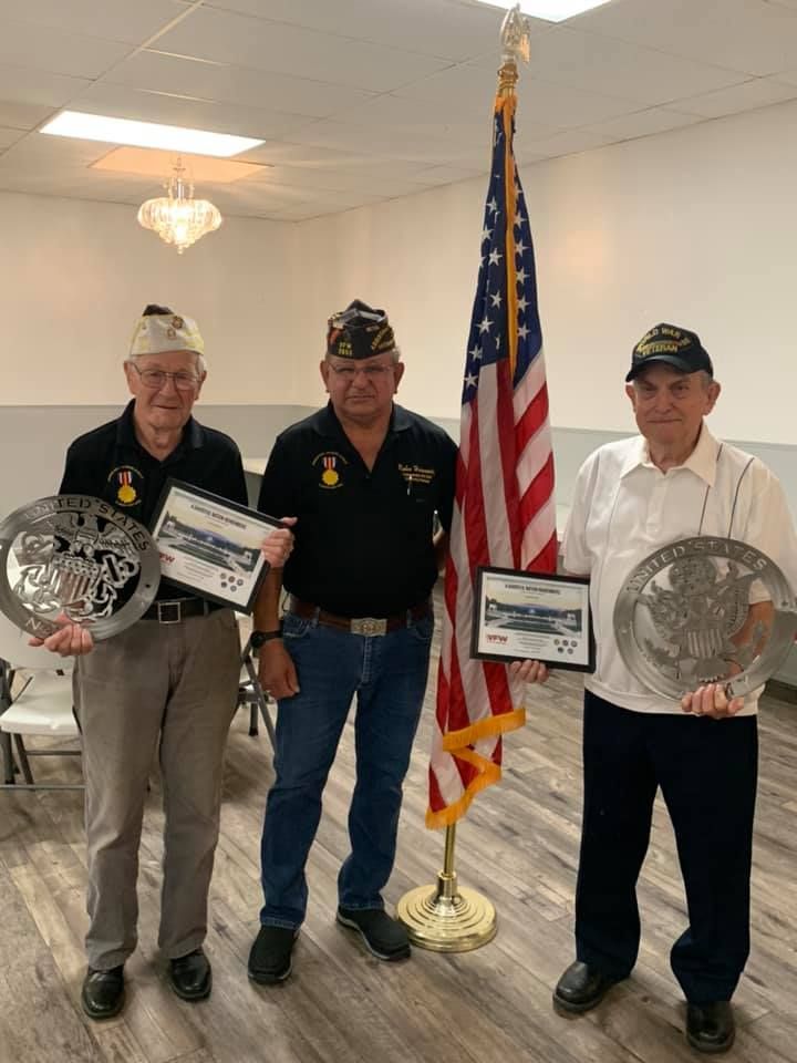 Three men are standing in front of an american flag holding plaques.