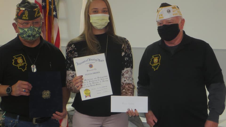 Two men and a woman wearing masks are standing next to each other holding a certificate and a check.