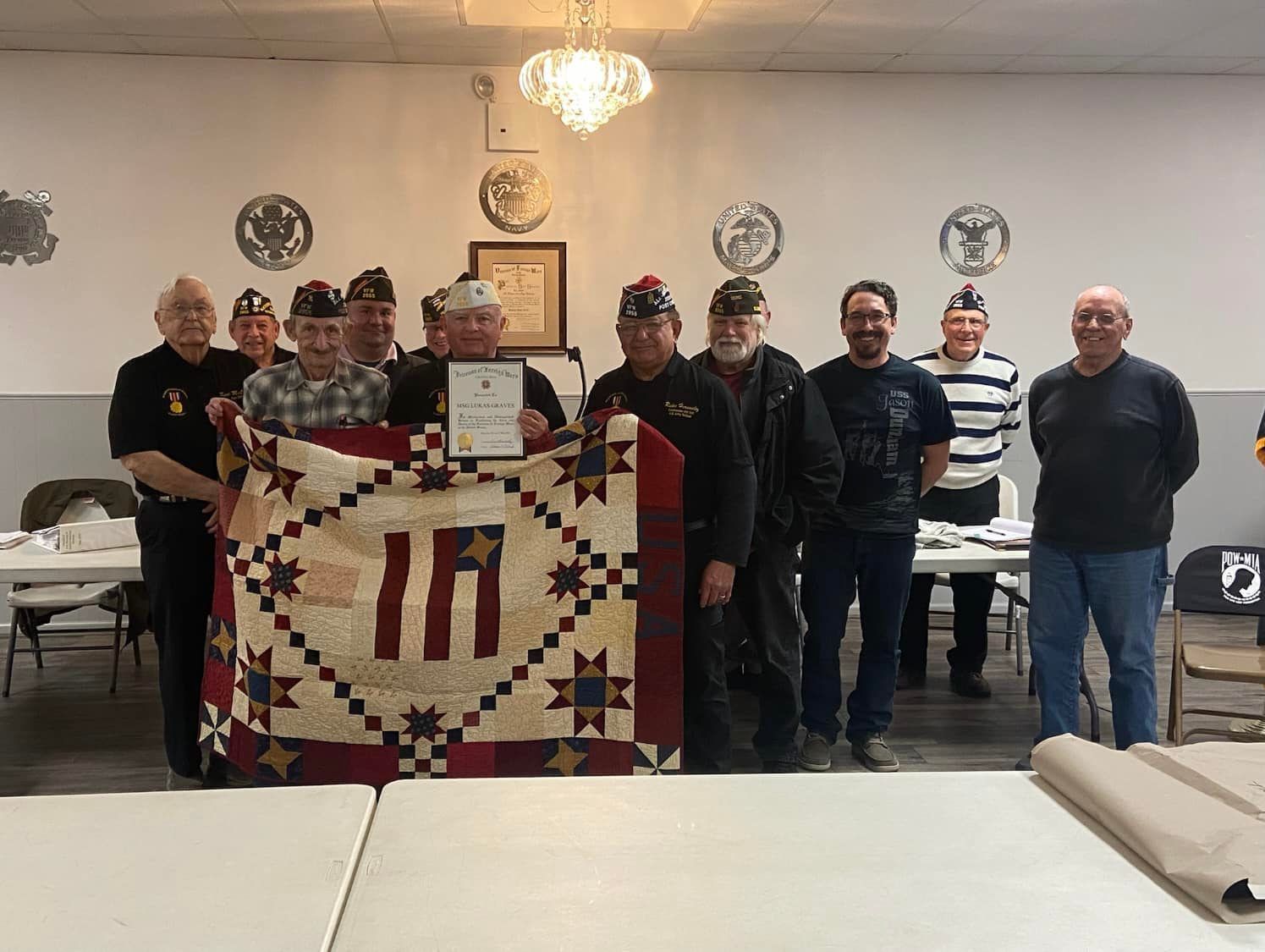 A group of men are standing around a table holding a quilt.