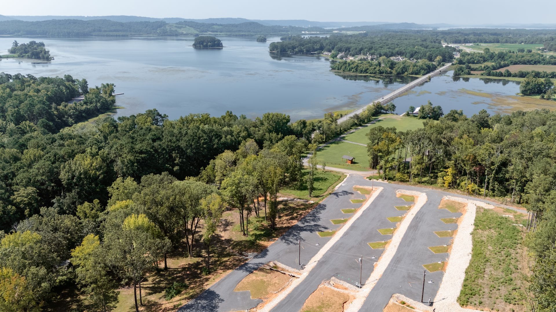 An aerial view of a lake surrounded by trees and a road.