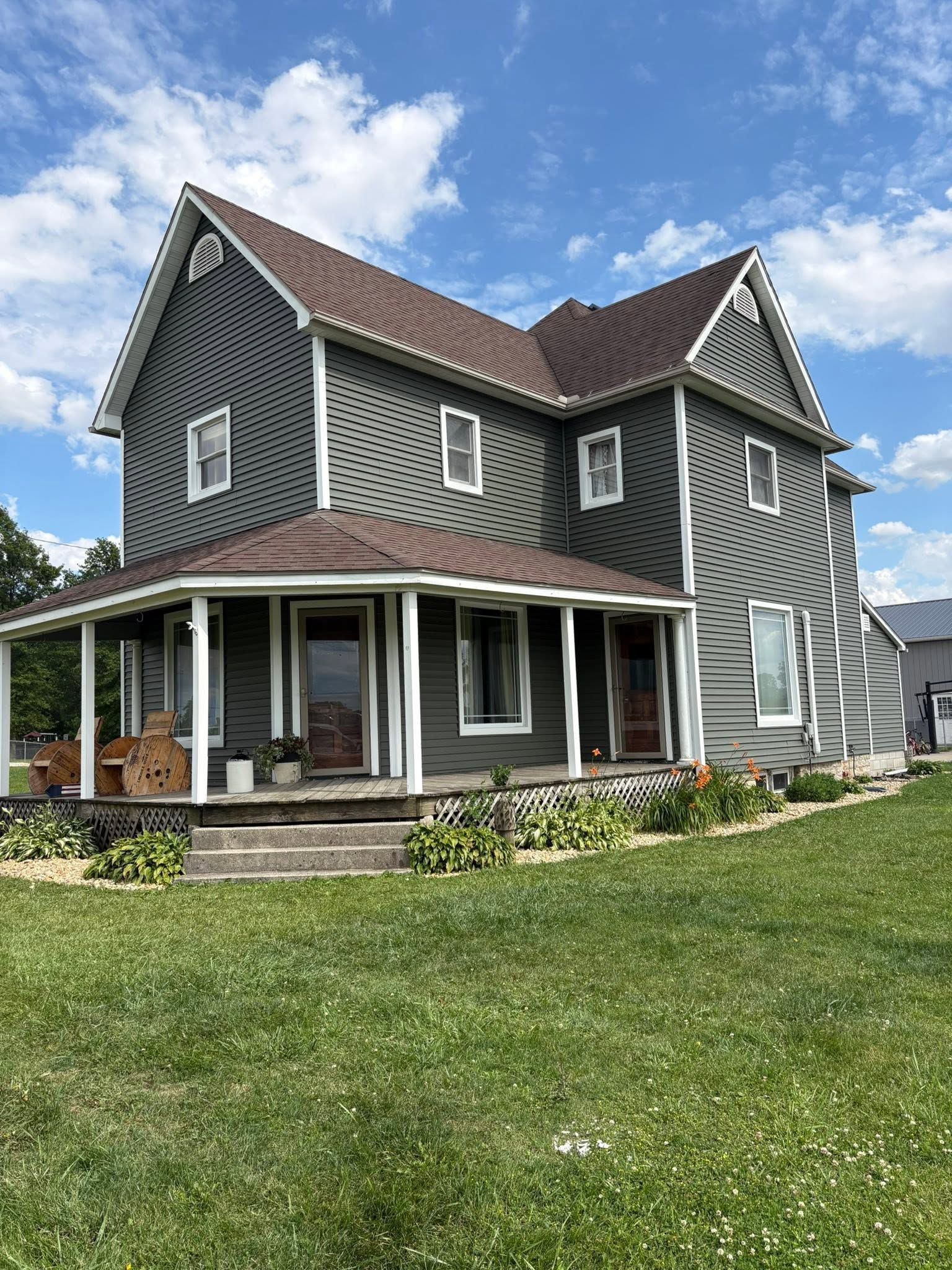 Gray two-story house with white trim and a covered porch on a green lawn under a blue sky