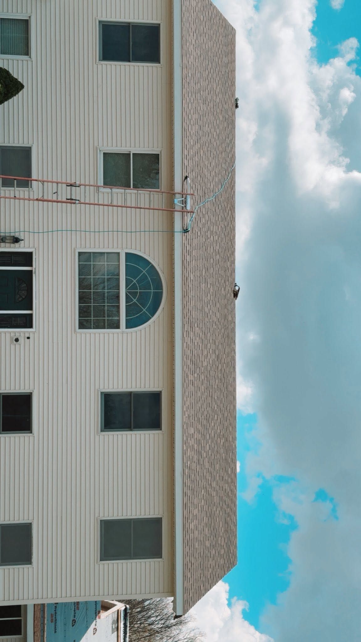 Tall apartment building facade under a bright blue sky with clouds, shown sideways in the frame