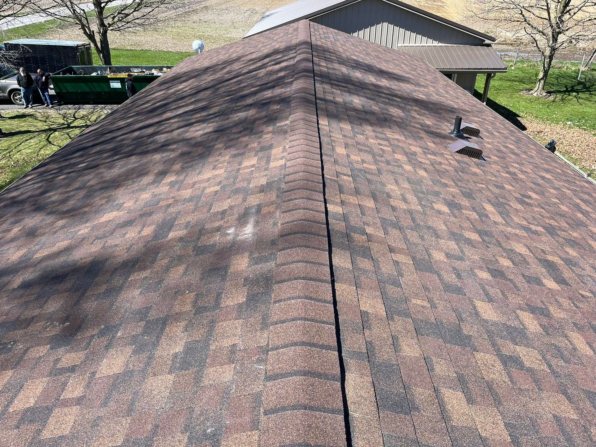 Close-up of a brown shingled roof with a ridge vent and a small roof fixture.