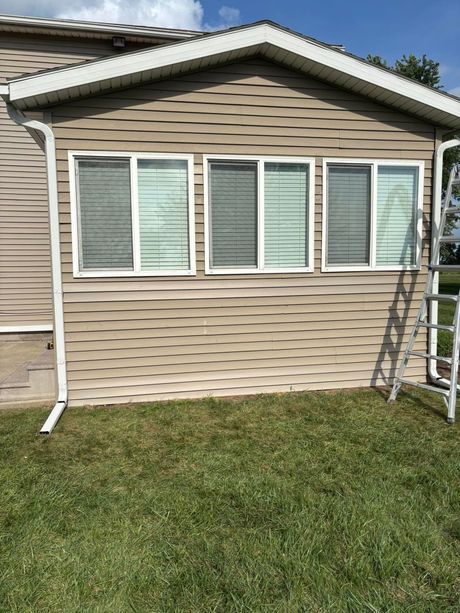 Tan house exterior with white-trimmed windows and a ladder leaning beside them over a grassy lawn