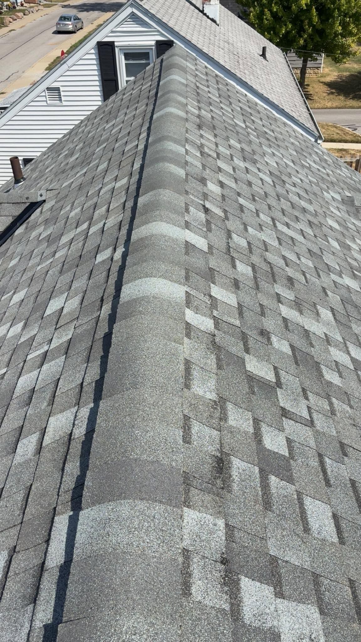 Roof covered in gray asphalt shingles, viewed from the ridge toward a dormer and street below.