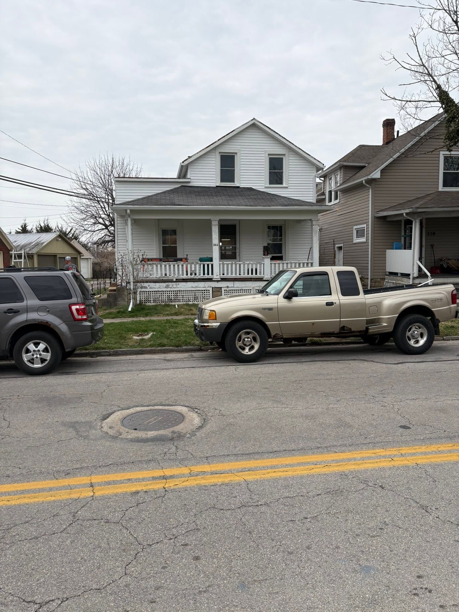 Two parked pickup trucks on a residential street in front of a white house with a porch.