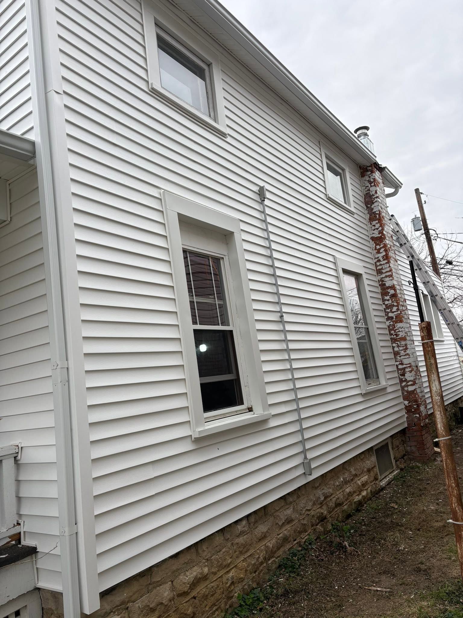 Side view of a white vinyl-sided house with windows and a narrow gravel strip along the foundation