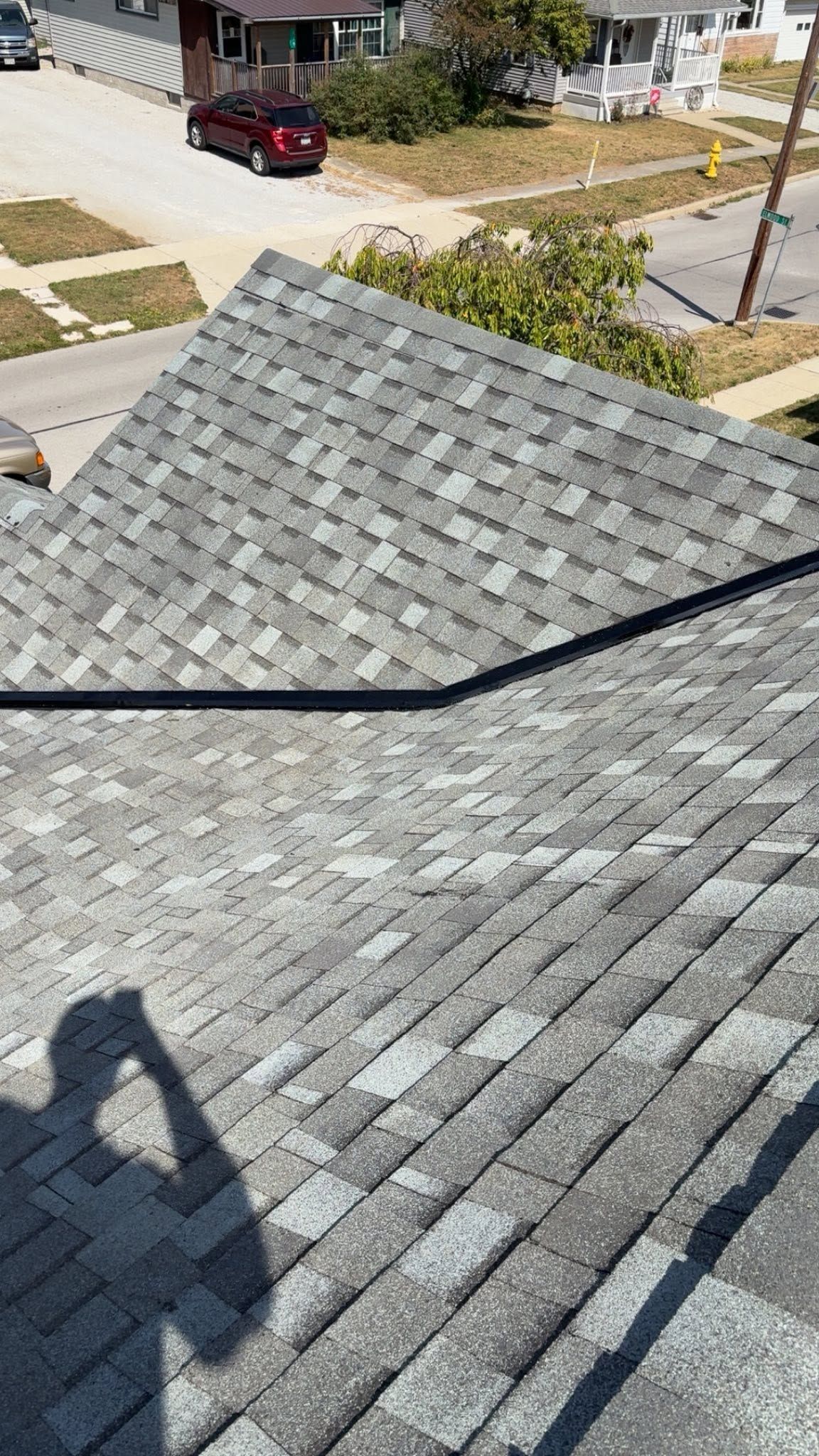 Gray shingle roof seen from above, with a street and parked red SUV in the background.