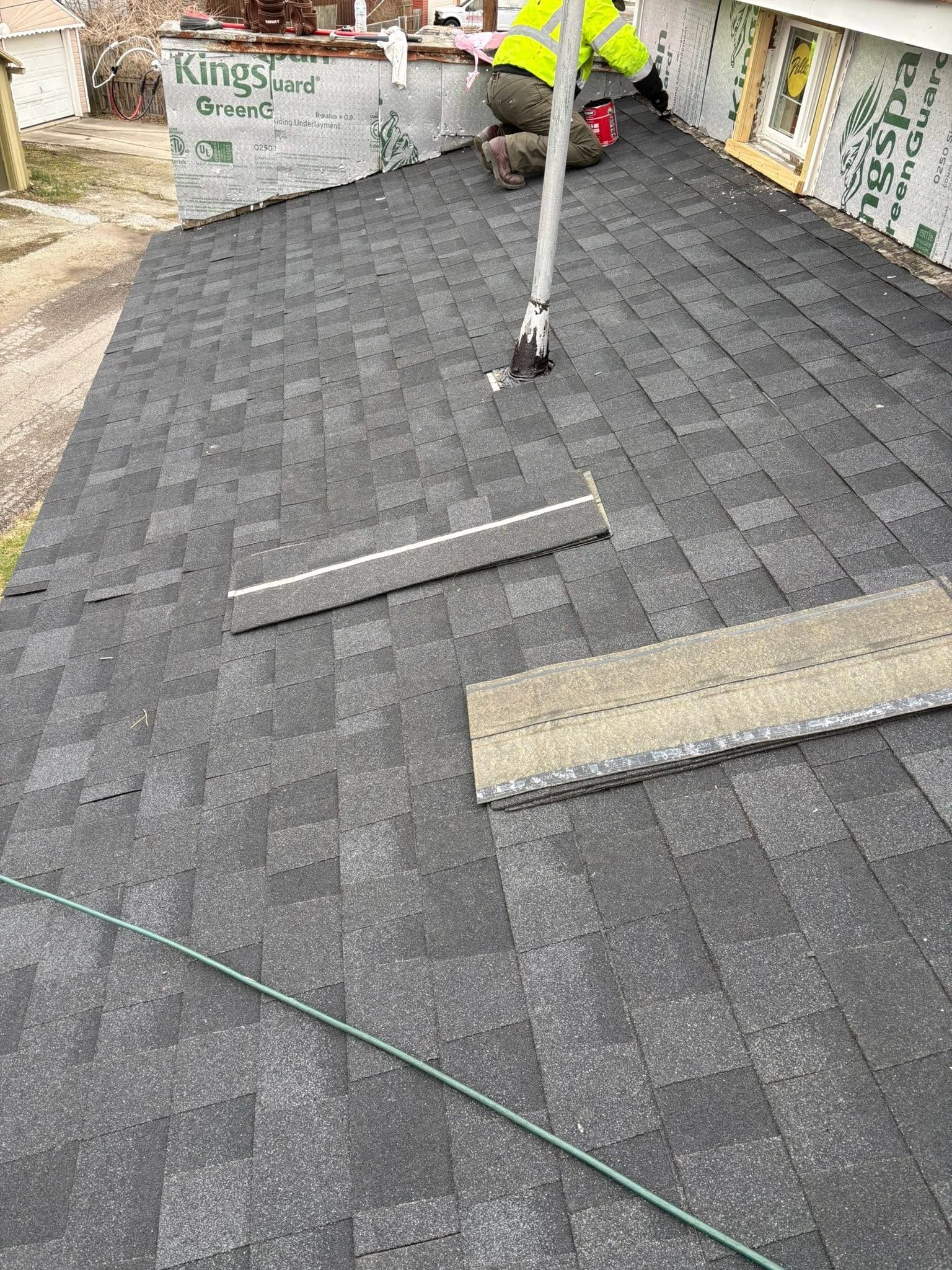Flat roof with gray shingles, a vent pipe, and wooden planks near a stone wall.
