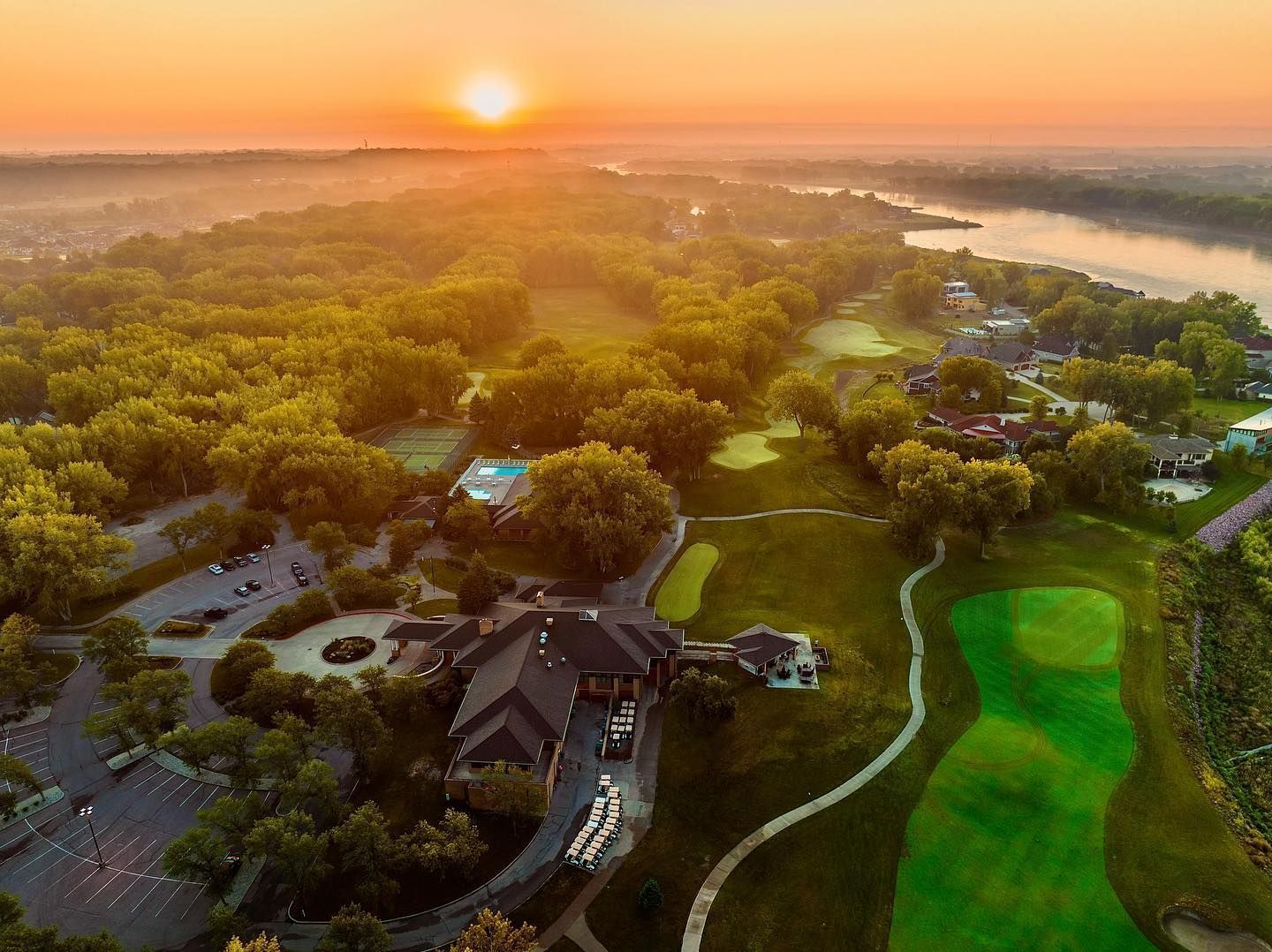 An aerial view of a golf course with a river in the background at sunset.