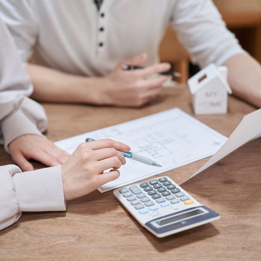 A man and a woman are sitting at a table using a calculator and a pen.