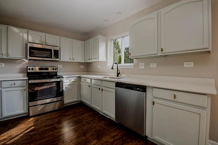 A modern kitchen with light green cabinets, stainless steel appliances, and dark wood floors.
