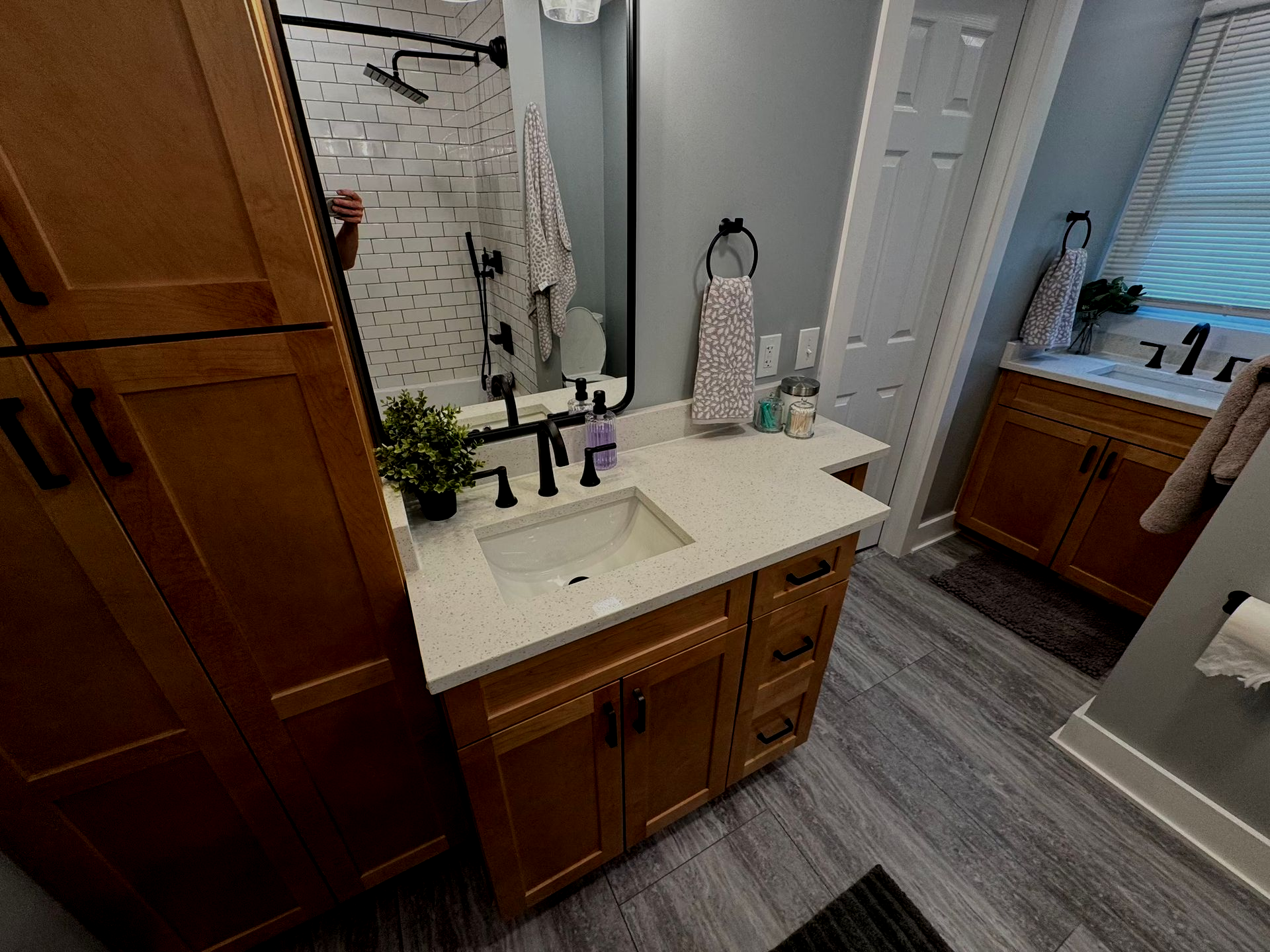 Bathroom with wooden cabinets, a sink, a mirror, and a shower. Gray and white color scheme.