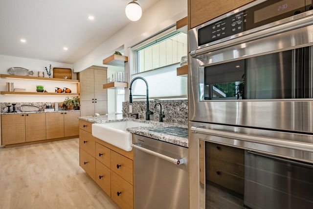 Bright modern kitchen with light wood cabinets, marble counters, and stainless steel appliances