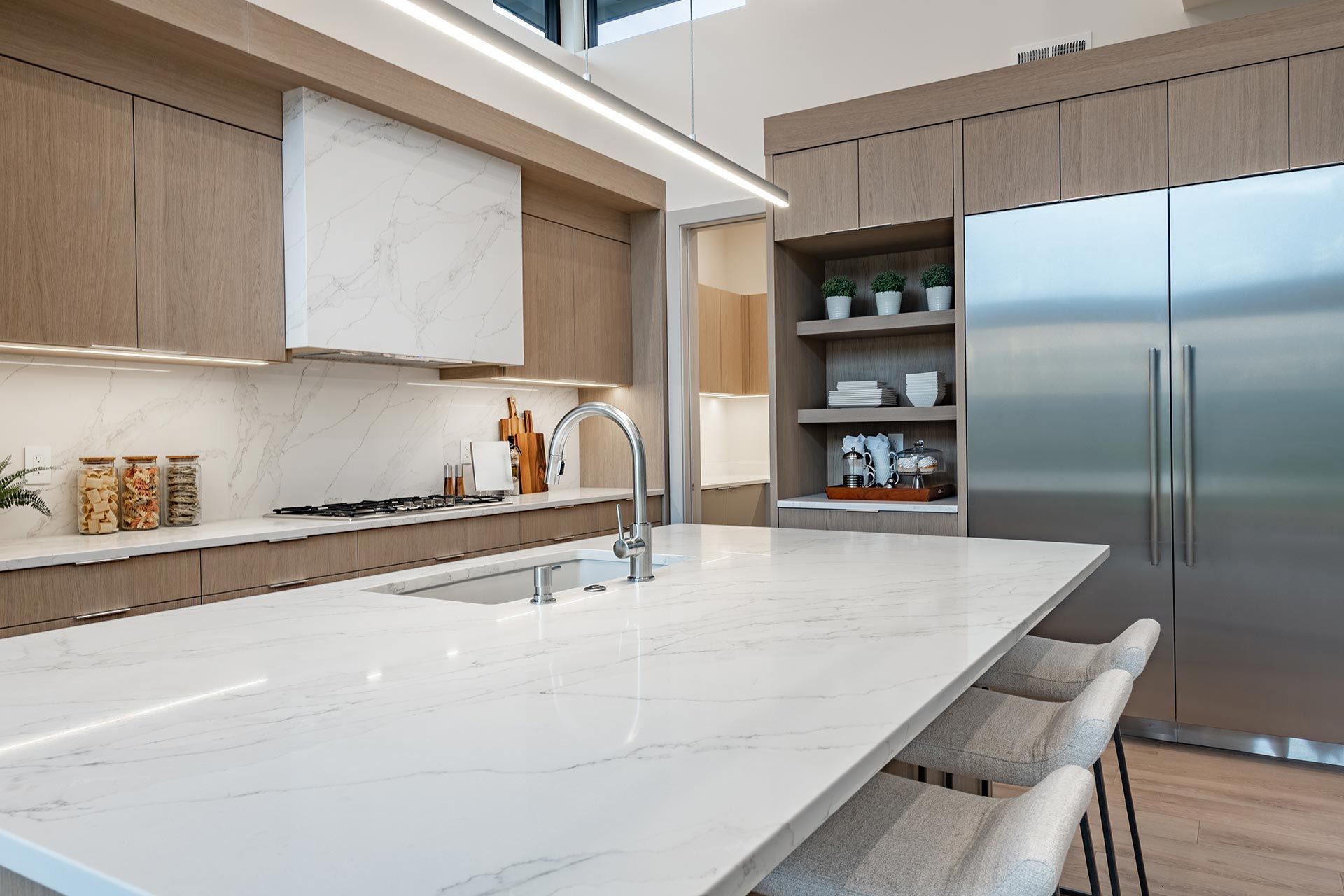 Modern kitchen with a large white island, wood cabinets, and stainless steel refrigerator