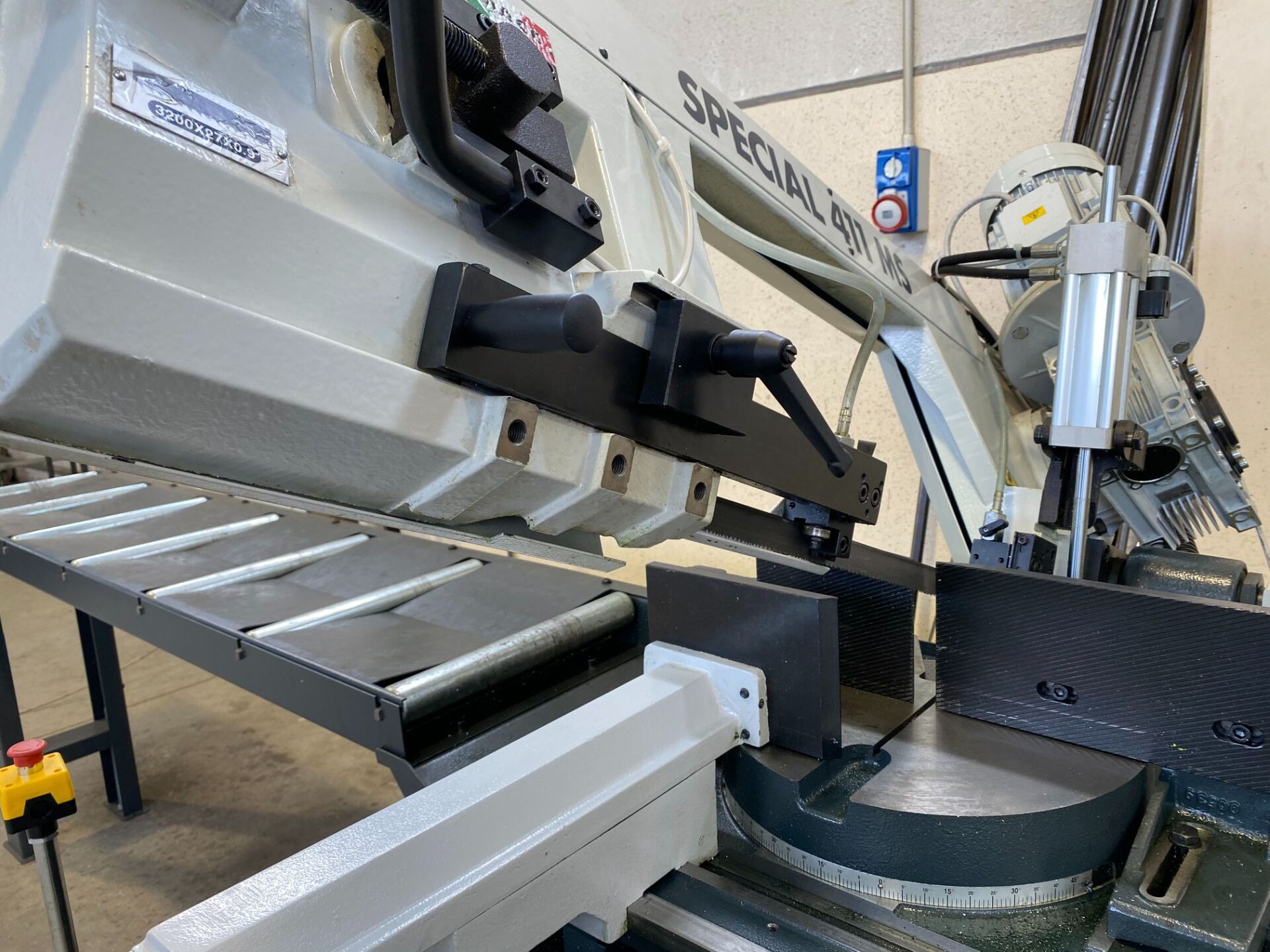 Sega a nastro, grigio chiaro, con parti nere, che taglia un blocco di metallo nero su un tavolo in un'officina.