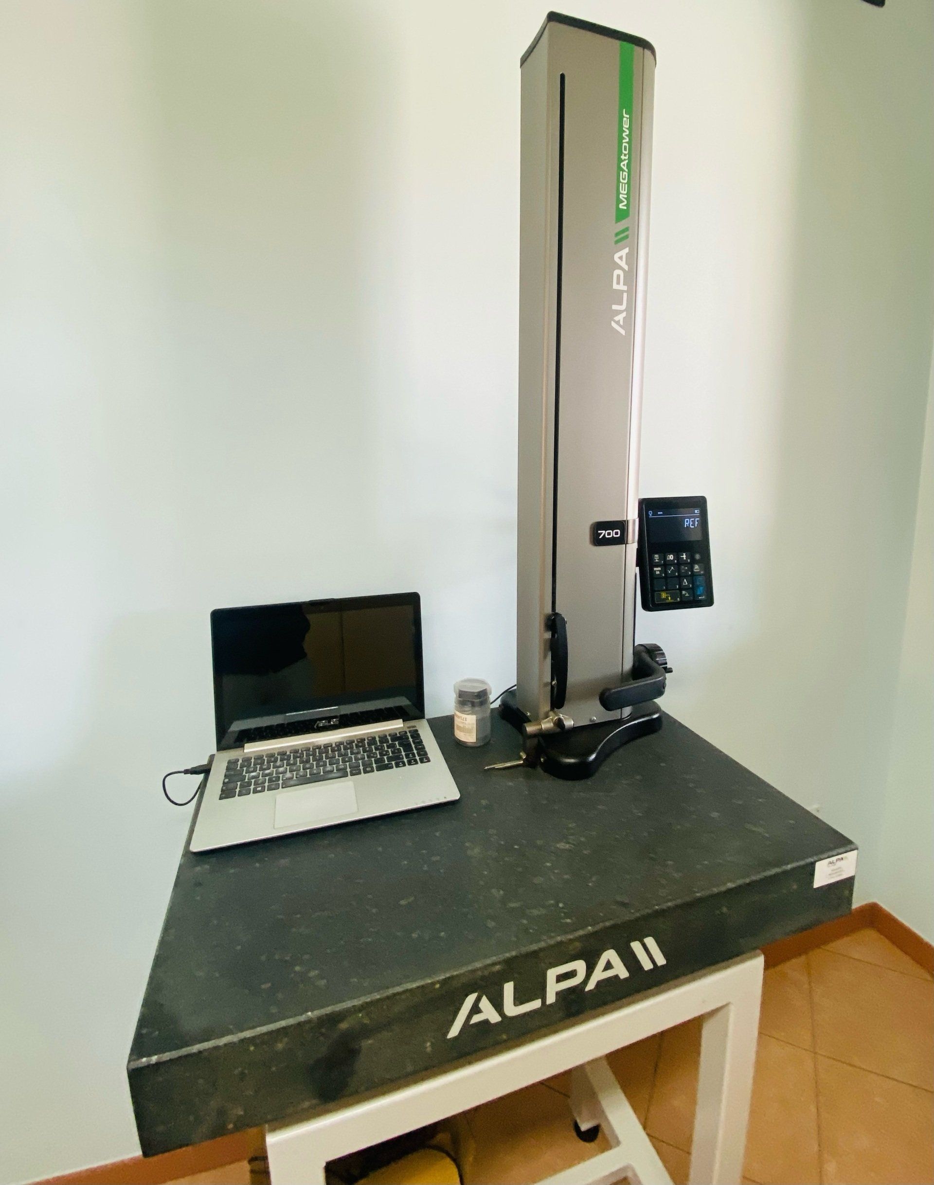 Un alto strumento di misurazione ALPA II grigio su un tavolo di granito nero con un computer portatile, in una stanza con pareti bianche.