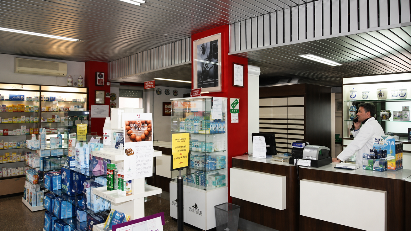 Bancone di un negozio con biglietti della lotteria, snack e scaffali; cassiere dietro la cassa in un minimarket.