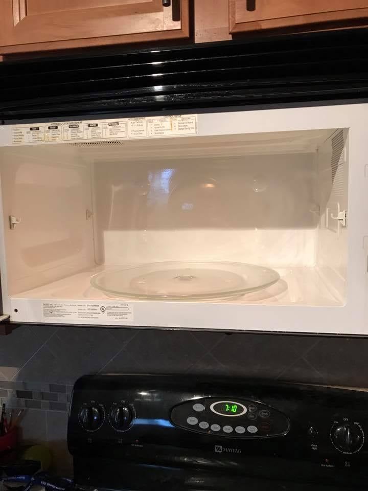 An open, empty microwave above a black stovetop. A glass plate is inside the microwave.