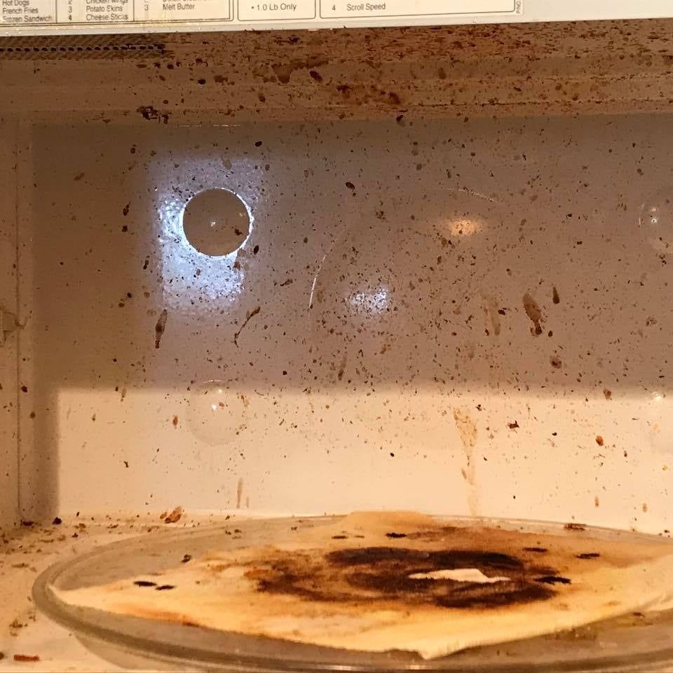 Dirty microwave interior with food splatters and a burnt plate.