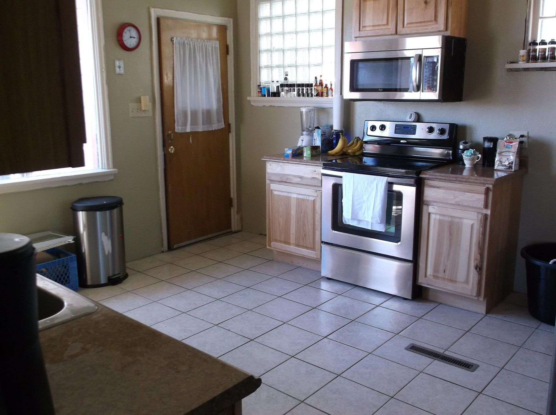 Kitchen with stainless steel appliances, light wood cabinets, and white tile flooring.