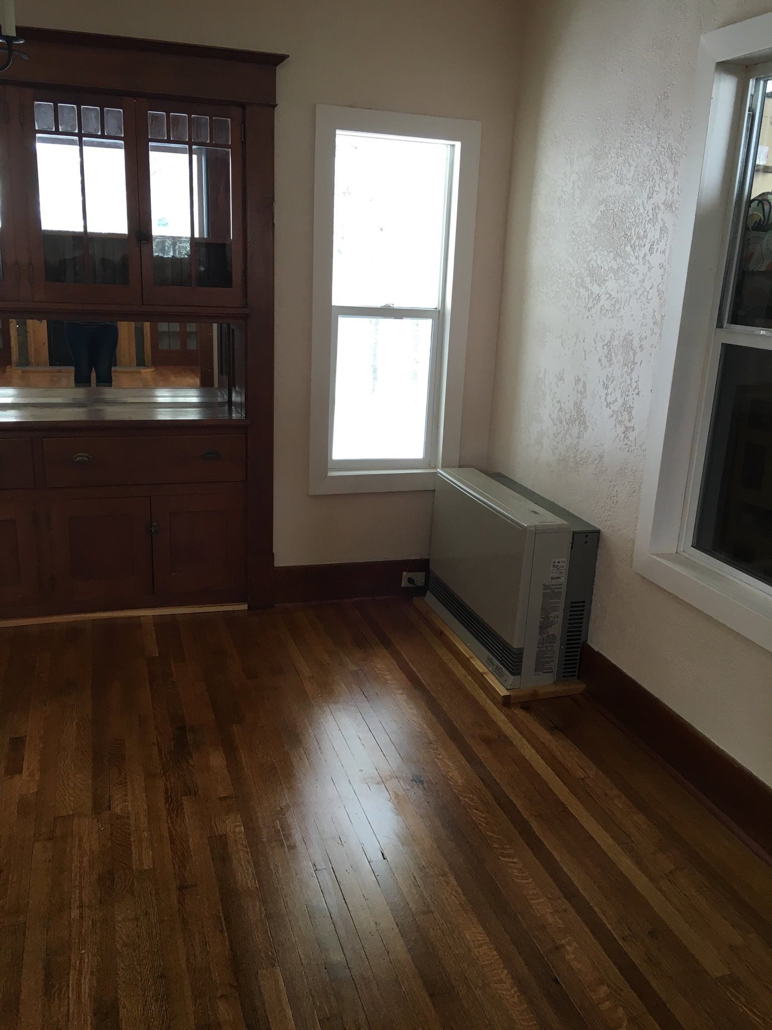 Hardwood floor in room with window and radiator. Wood cabinet with frosted glass.
