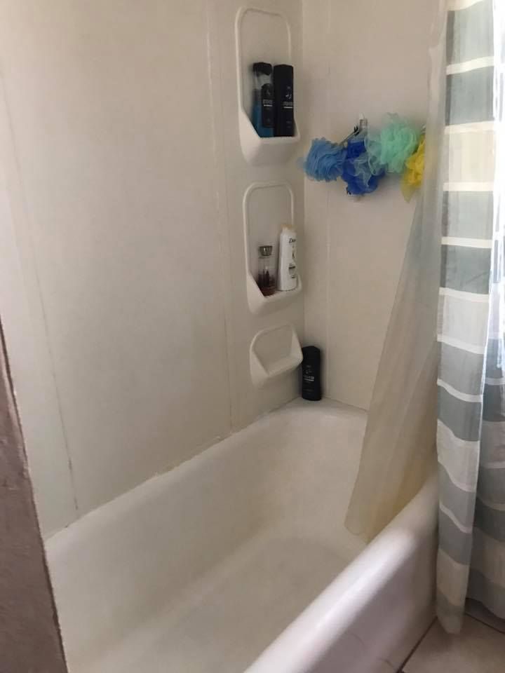 White bathtub and shower enclosure with shower products on shelves.