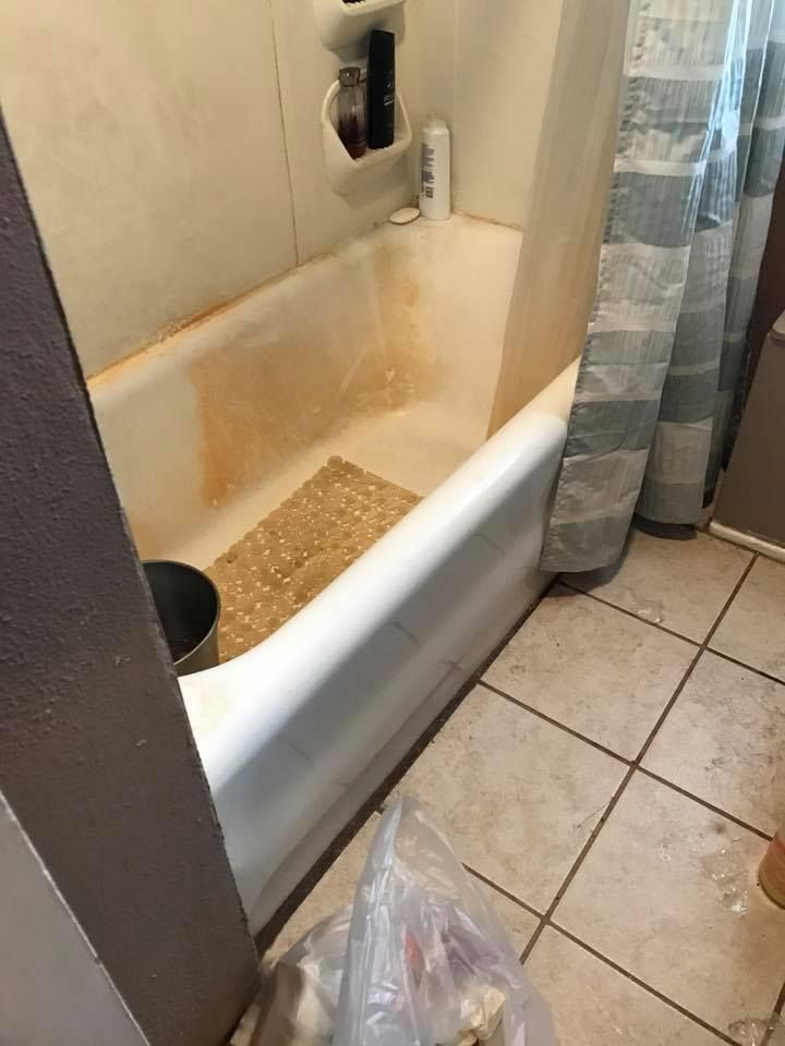 Dirty, stained white bathtub with orange discoloration, and a patterned bath mat.