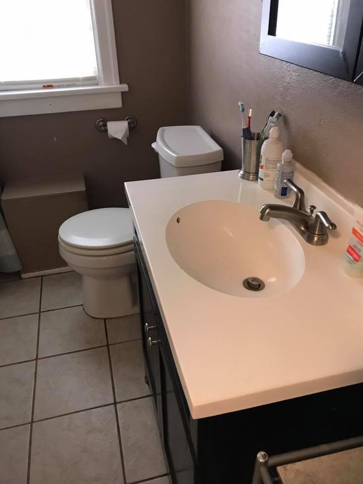 Small bathroom with a sink, toilet, and window. White countertop and beige walls.