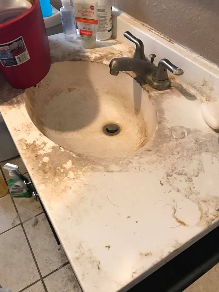 Dirty bathroom sink with dark stains, faucet, and cleaning supplies.