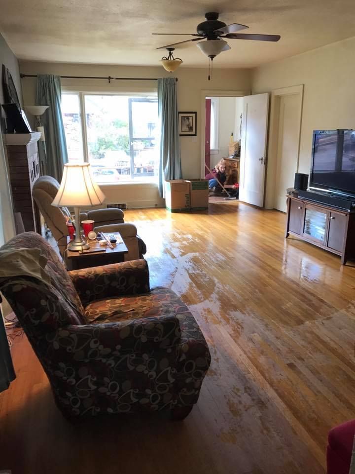 Living room with water damage on hardwood floor, furniture, and doorway to another room.