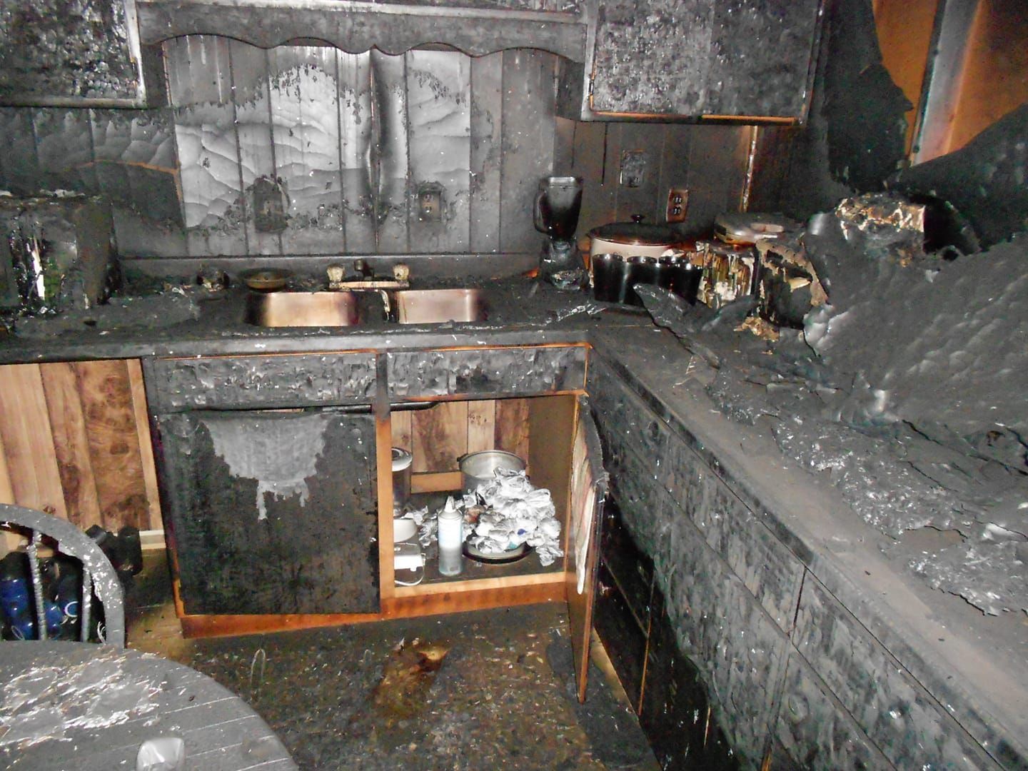 Burned kitchen interior; cabinets, countertops, and appliances are severely charred.