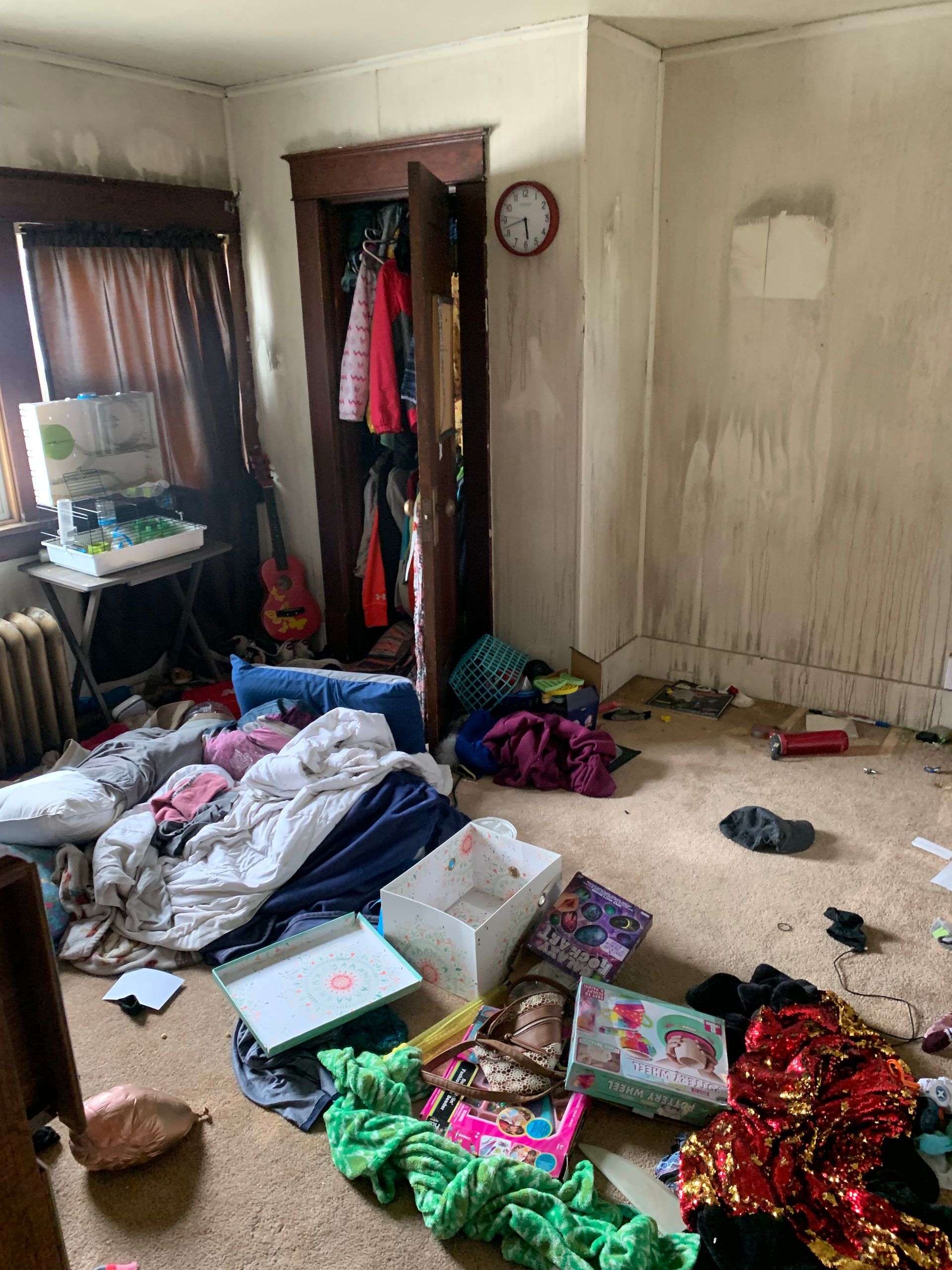 Cluttered room with clothes, toys, and debris scattered across the floor and walls with soot. A closet door is ajar.