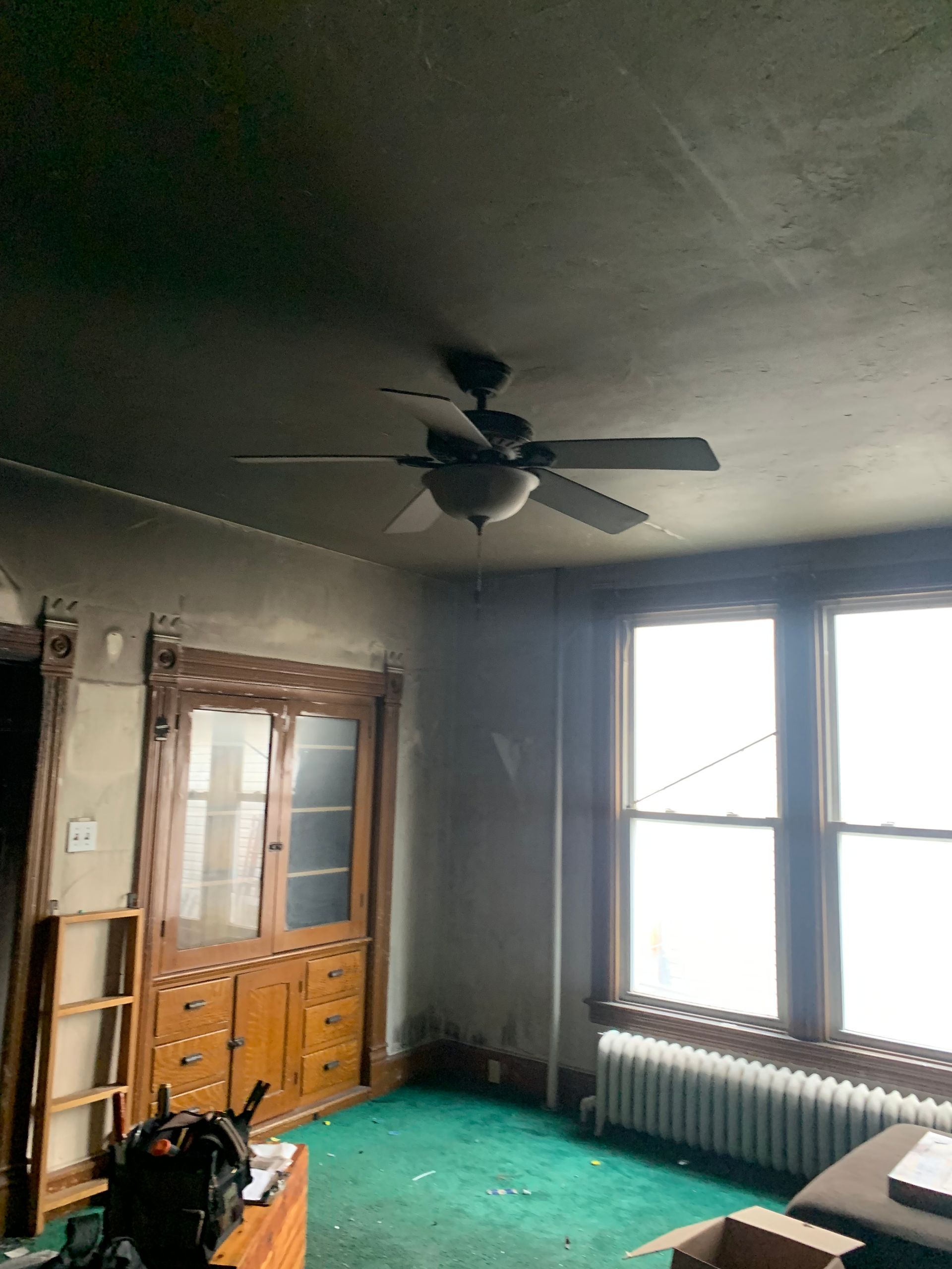 Room interior with a ceiling fan, wooden cabinets, and green carpet.