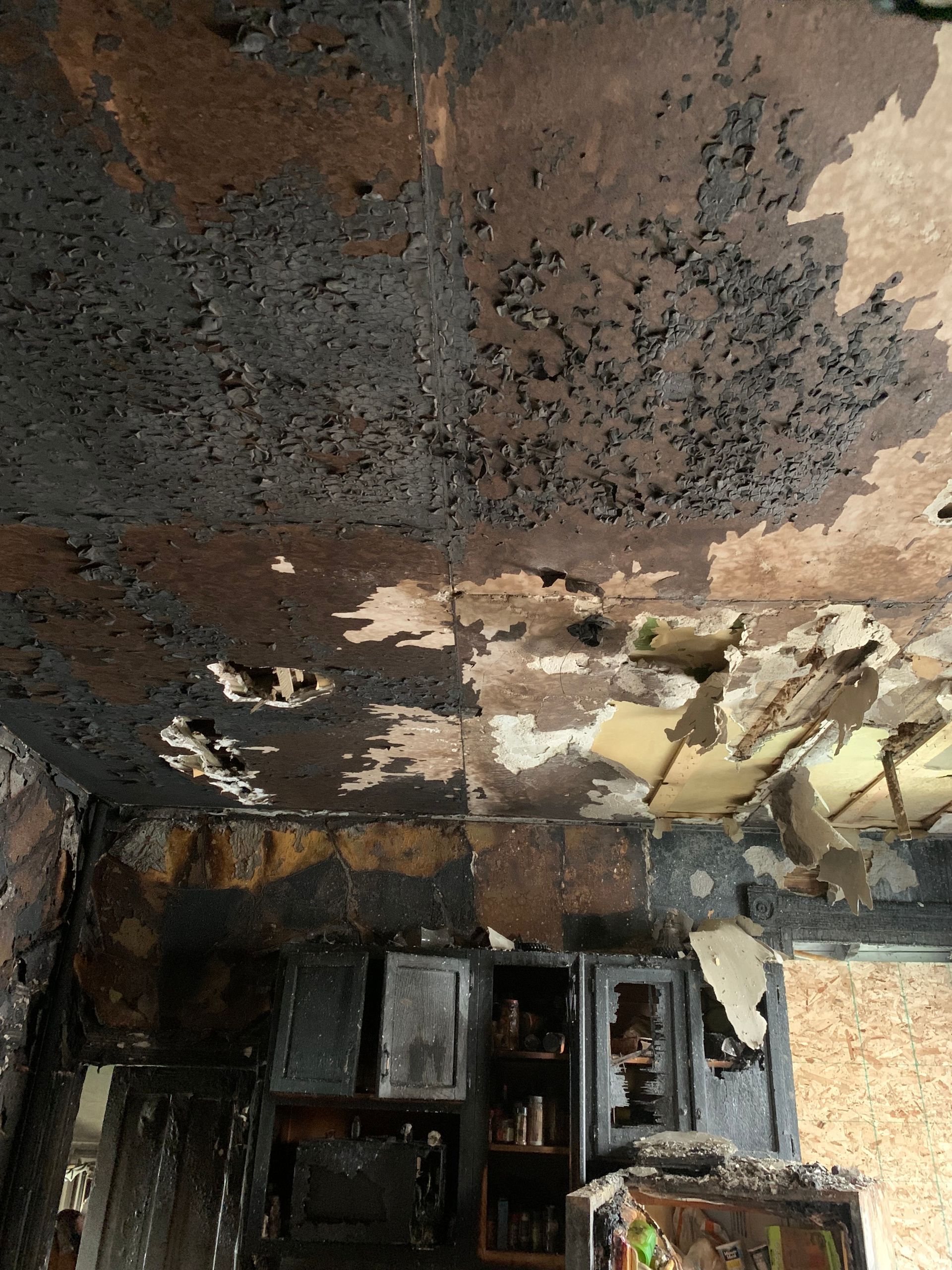 Charred kitchen ceiling and cabinets damaged by fire.