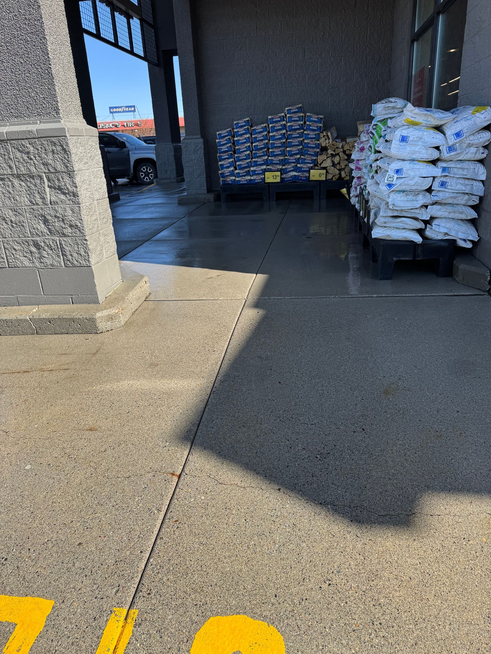 Concrete sidewalk with bags of ice and firewood near a store entrance.
