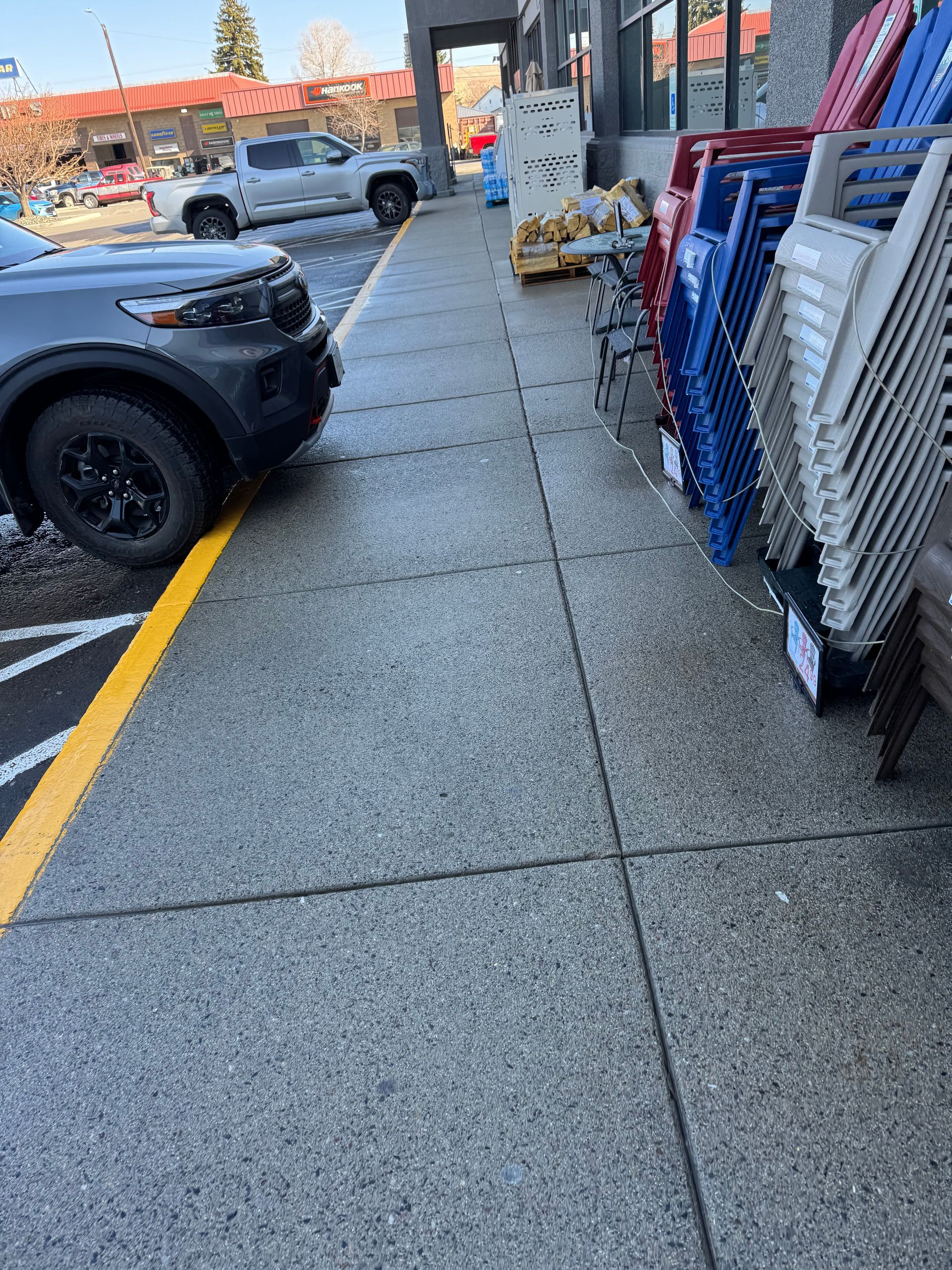Sidewalk with car parked on the edge, a row of chairs lining the building.