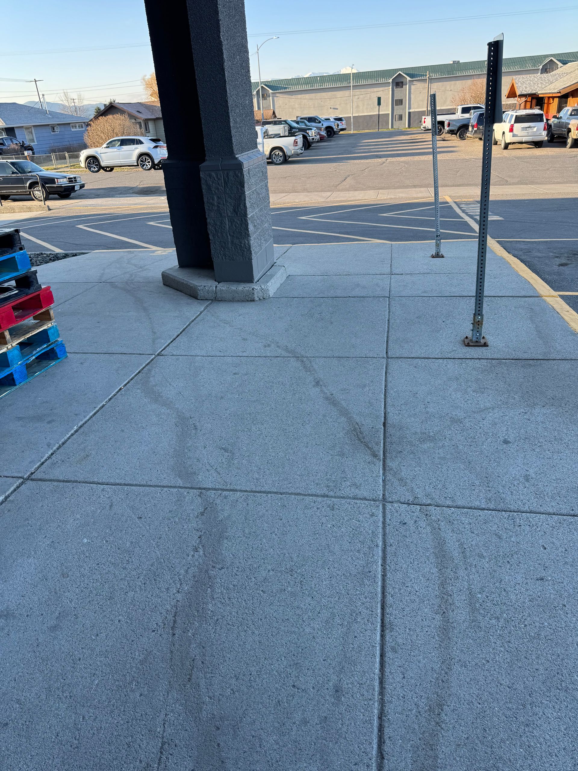 Sidewalk outside a building with tire tracks, parking lot in background.