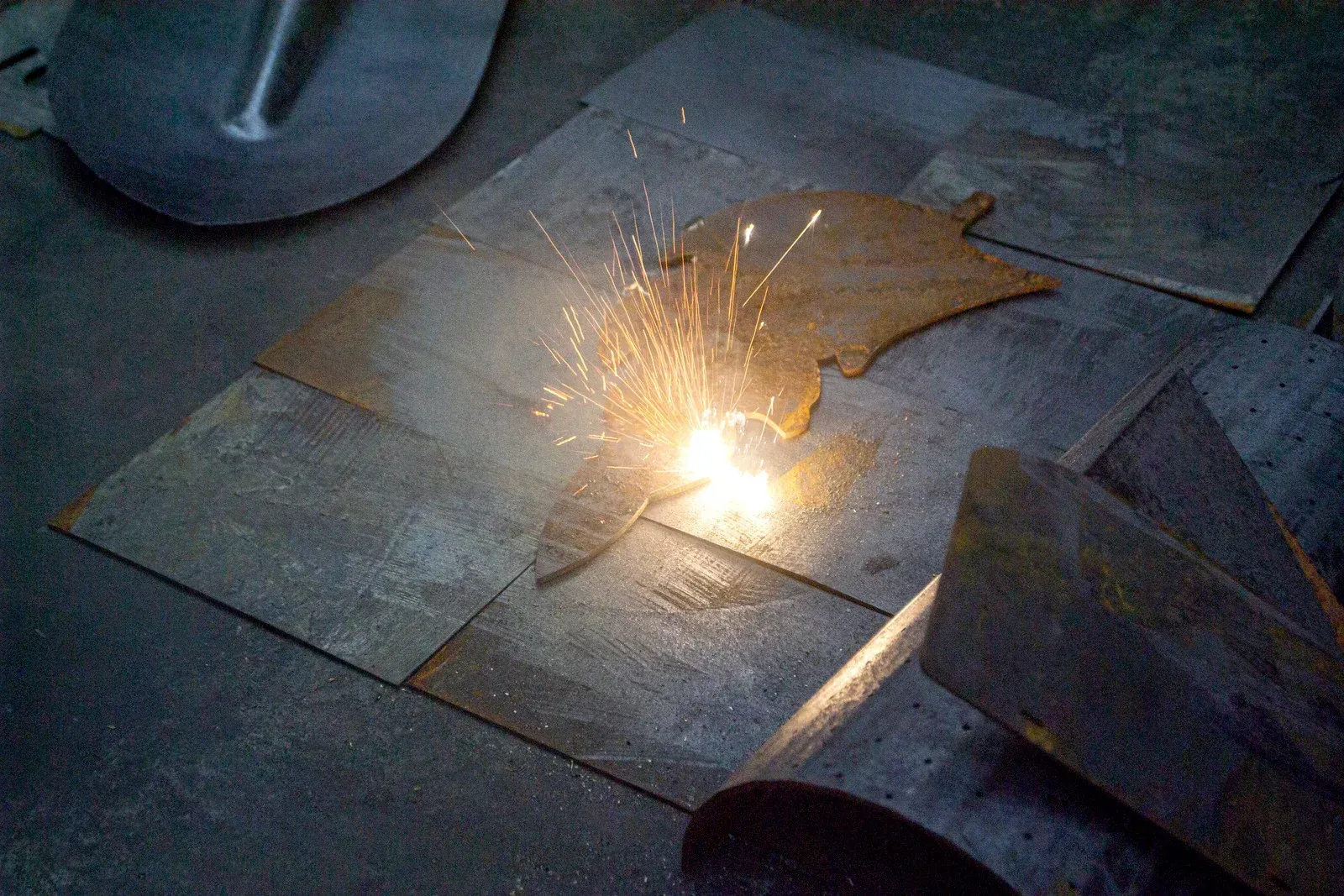 Sparks fly from a metal pig shape being cut on a metal surface.