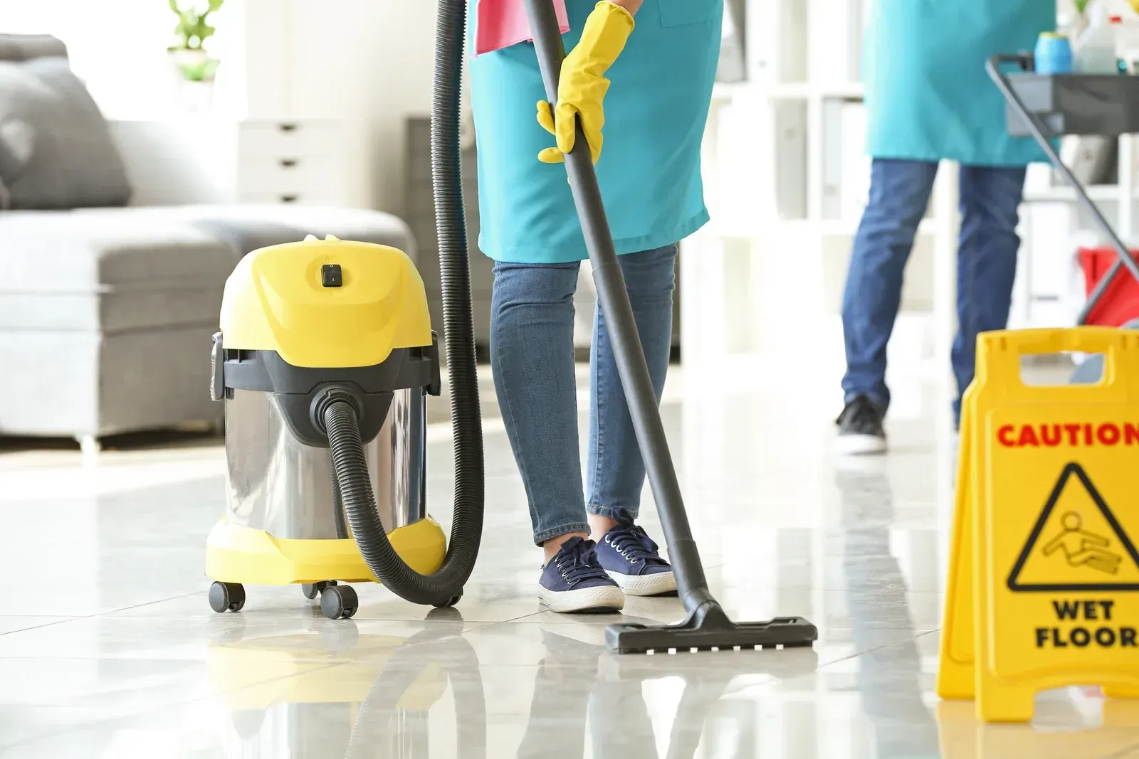 Two cleaners mopping a floor. Yellow vacuum and wet floor sign present.