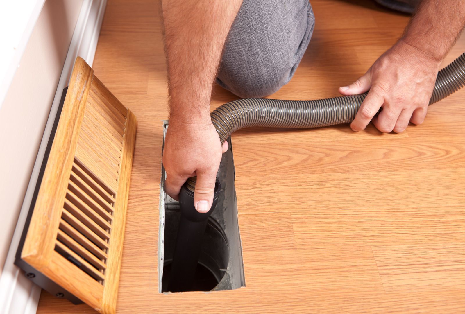 Person vacuuming a floor vent in a wooden floor.
